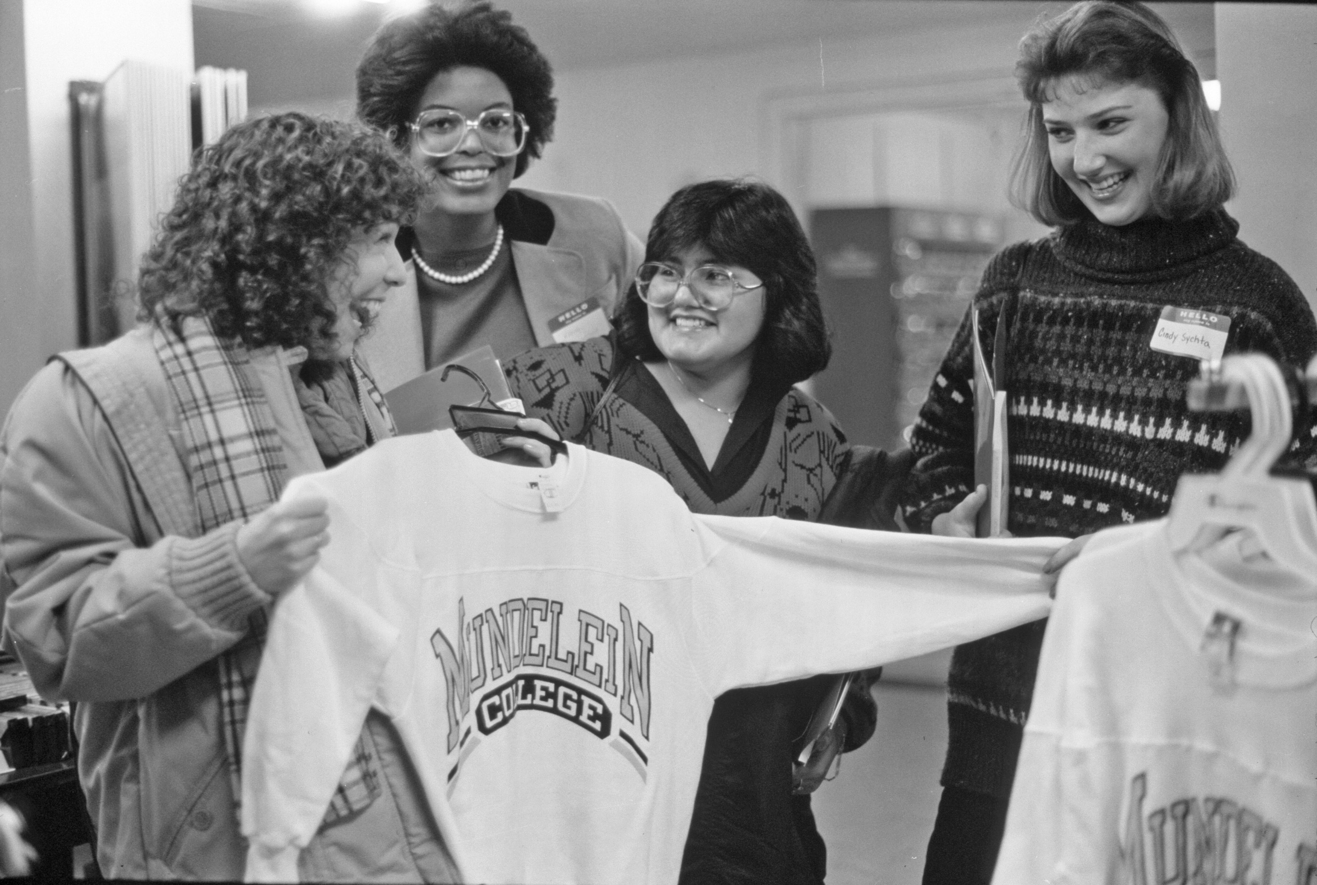 Four students holding a Mundelein College crew neck